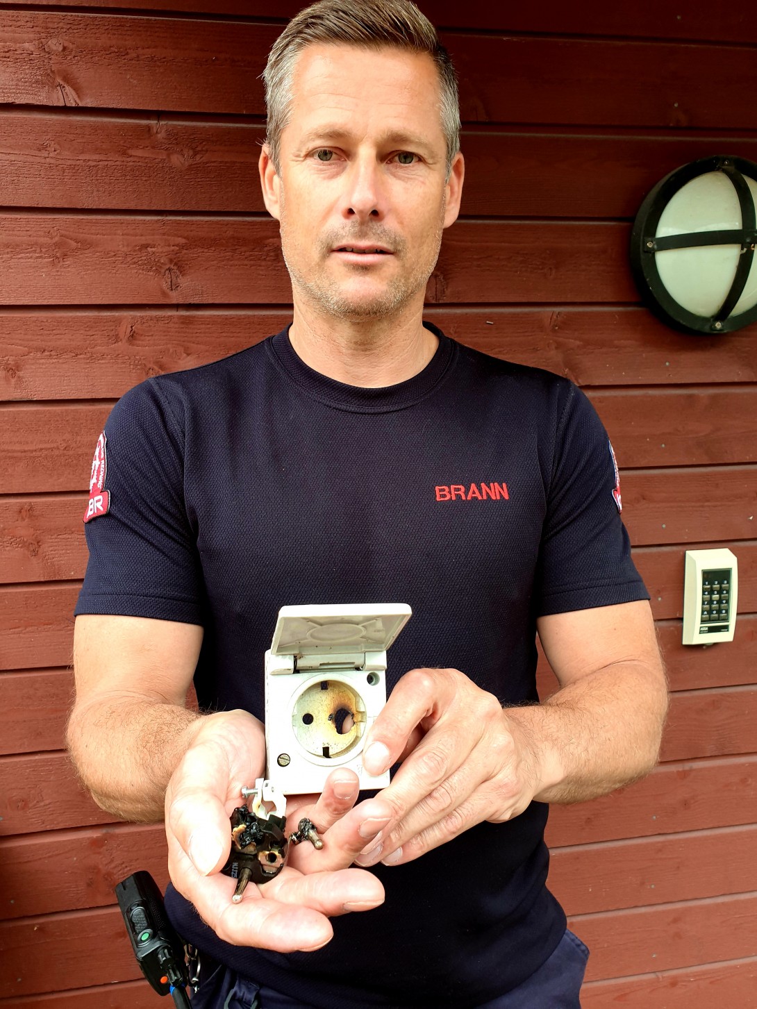 Brannformann Morten Nygaard viser frem stikkontakten som  begynte å brenne på utsiden av huset hans.